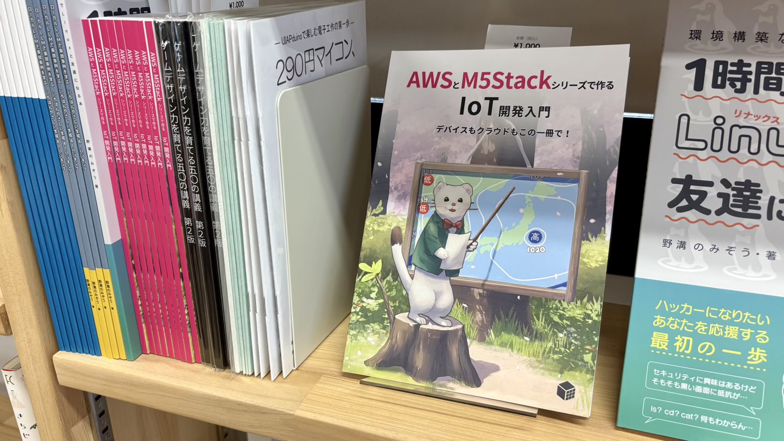 技術同人誌販売の本棚の風景の写真。『AWSとM5Stackシリーズで作るIoT開発入門』が面陳されている